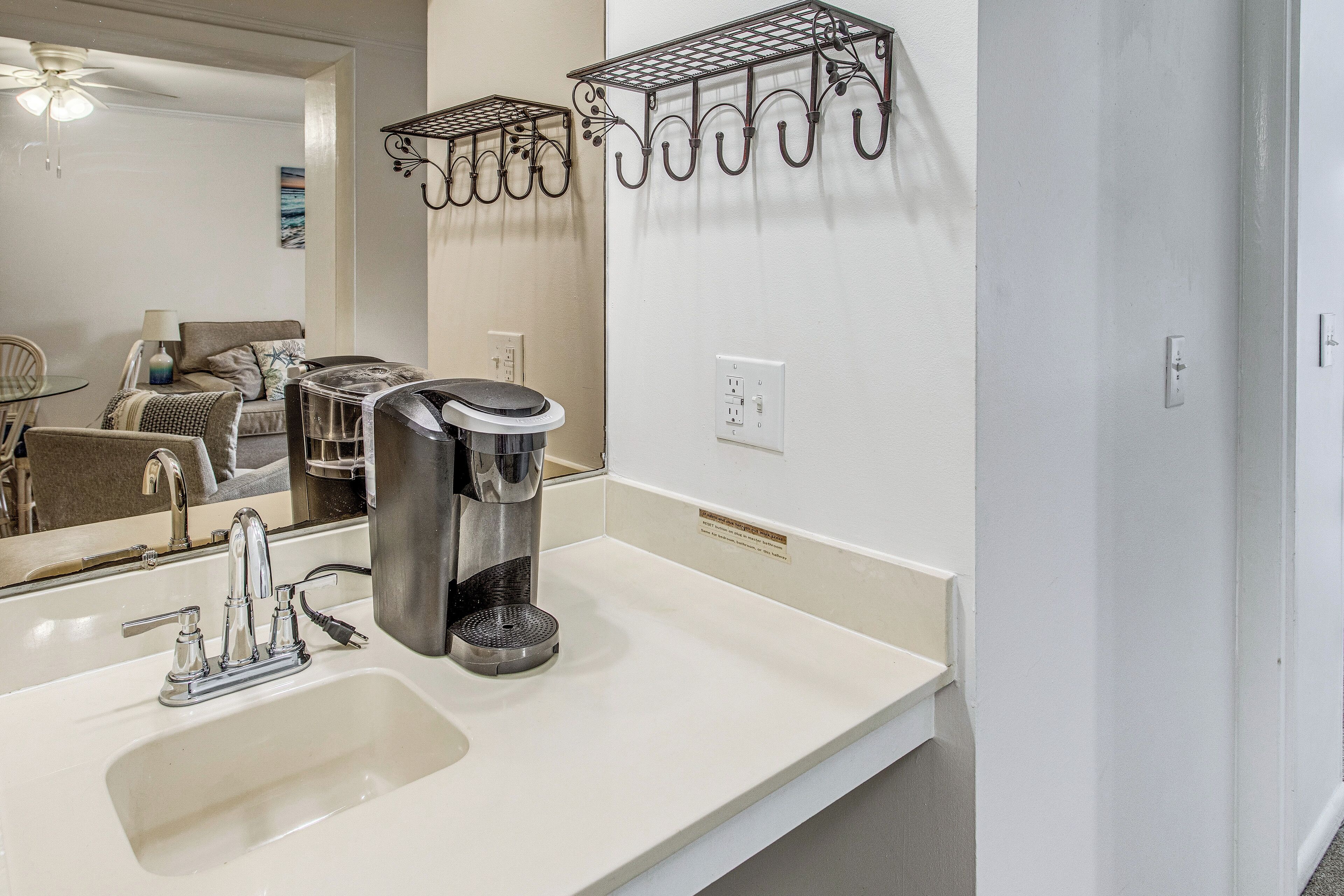 A bathroom with a sink, a coffee maker, a mirror, and a towel rack.