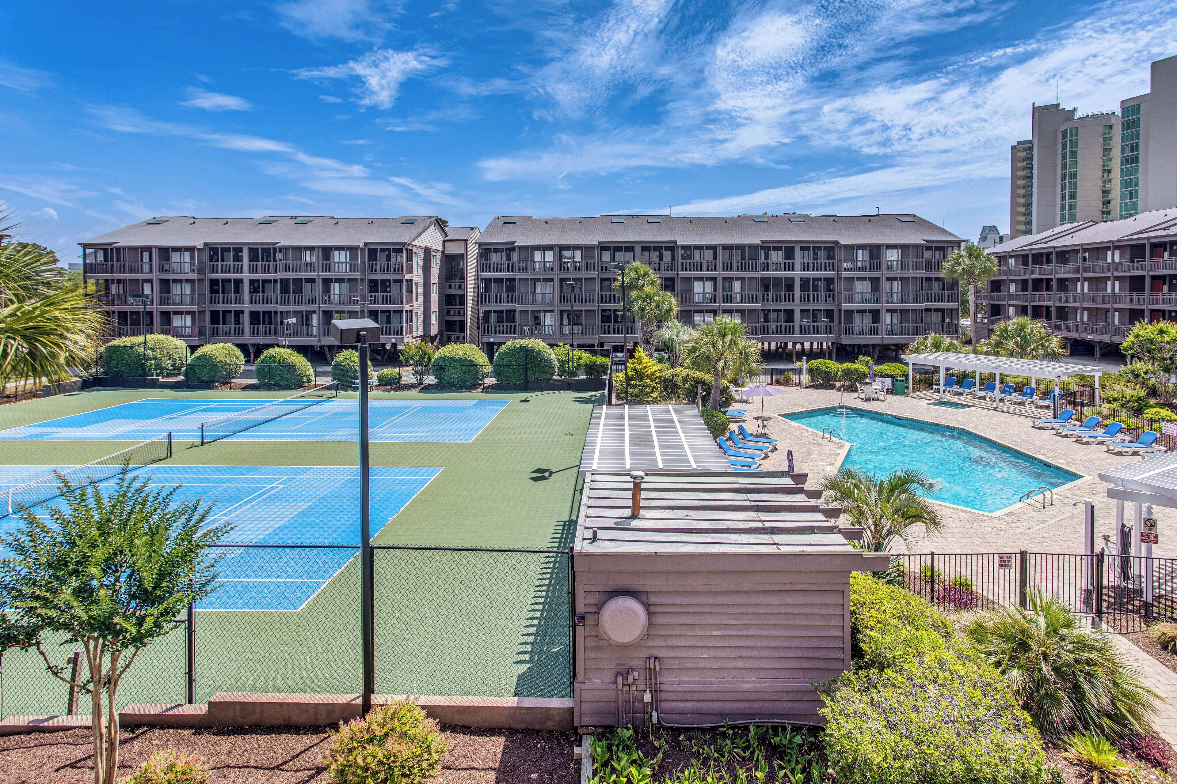 A hotel with multiple tennis courts, a swimming pool, and a covered seating area.