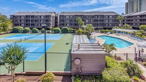 Un hotel con varias canchas de tenis, piscina y una zona de estar cubierta.