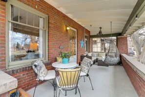 A brick building with a covered patio area featuring outdoor seating, a round table, and a hanging chair.