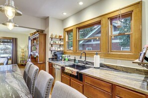 A kitchen with wooden cabinets, a marble countertop, a sink, and a dining area with chairs. - Explore Denver! Welcoming Home w/ Porch & Yard (Denver)