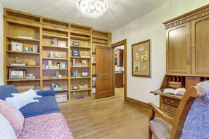 A room with a large wooden bookshelf, a desk with drawers, a blue sofa, and a patterned chair. - Explore Denver! Welcoming Home w/ Porch & Yard (Denver)