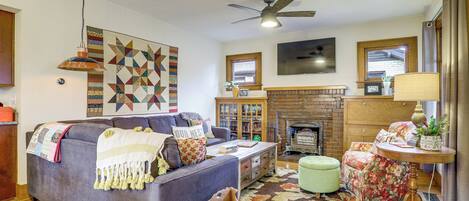 A living room with a sofa, a coffee table, a fireplace, and a ceiling fan.