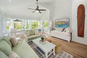 A spacious living area with a sofa, coffee table, and a painting of a landscape. - Happy Shack - Heart of Hanalei (Hanalei)