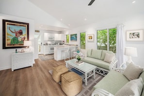 A modern living room with a sofa, coffee table, and wicker ottomans. - Happy Shack - Heart of Hanalei (Hanalei)