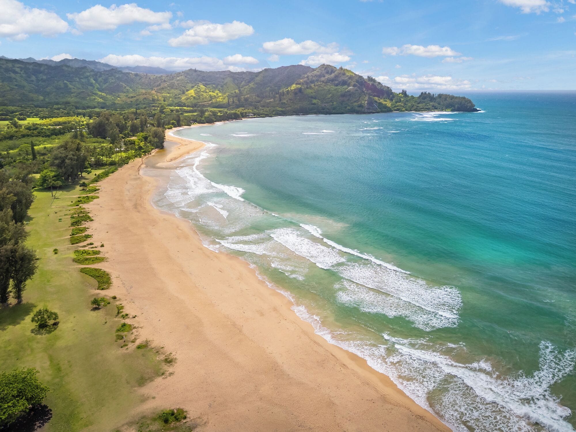A beach with clear waters, a sandy shore, and a mountainous backdrop.