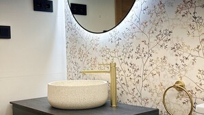 A bathroom with a round sink, a gold faucet, a towel ring, and a mirror.