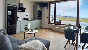 A modern kitchen with a large window, a dining area with a table and chairs, and a living room with a sofa.