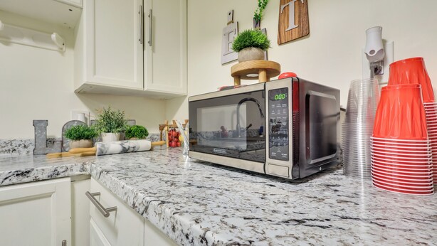 A kitchen with white cabinets, a granite countertop, a microwave, a coffee maker, and red plastic cups. - Retreat w/ Yard Near NYC & Metlife Stadium! (Teaneck)