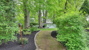 A brick pathway leading through a garden with trees and a bird feeder. - Retreat w/ Yard Near NYC & Metlife Stadium! (Teaneck)