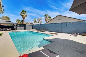 Ein Swimmingpool mit klarem Wasser, umgeben von einer Terrassenfläche mit Liegestühlen und einer überdachten Sitzgelegenheit.