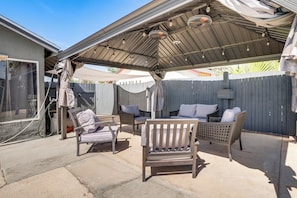 Eine Terrasse im Freien mit überdachter Sitzgruppe, Holzparkanlage und einem Haus im Hintergrund.
