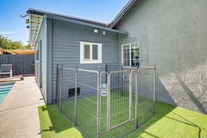 A fenced outdoor area with artificial grass, a pool, and a building with a window and a door.