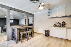 A kitchen with wooden flooring, a bar area with stools, white cabinets, and a ceiling fan.