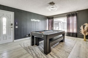 A pool table in a room with dark walls, a patterned rug, and a door with a frosted glass window.