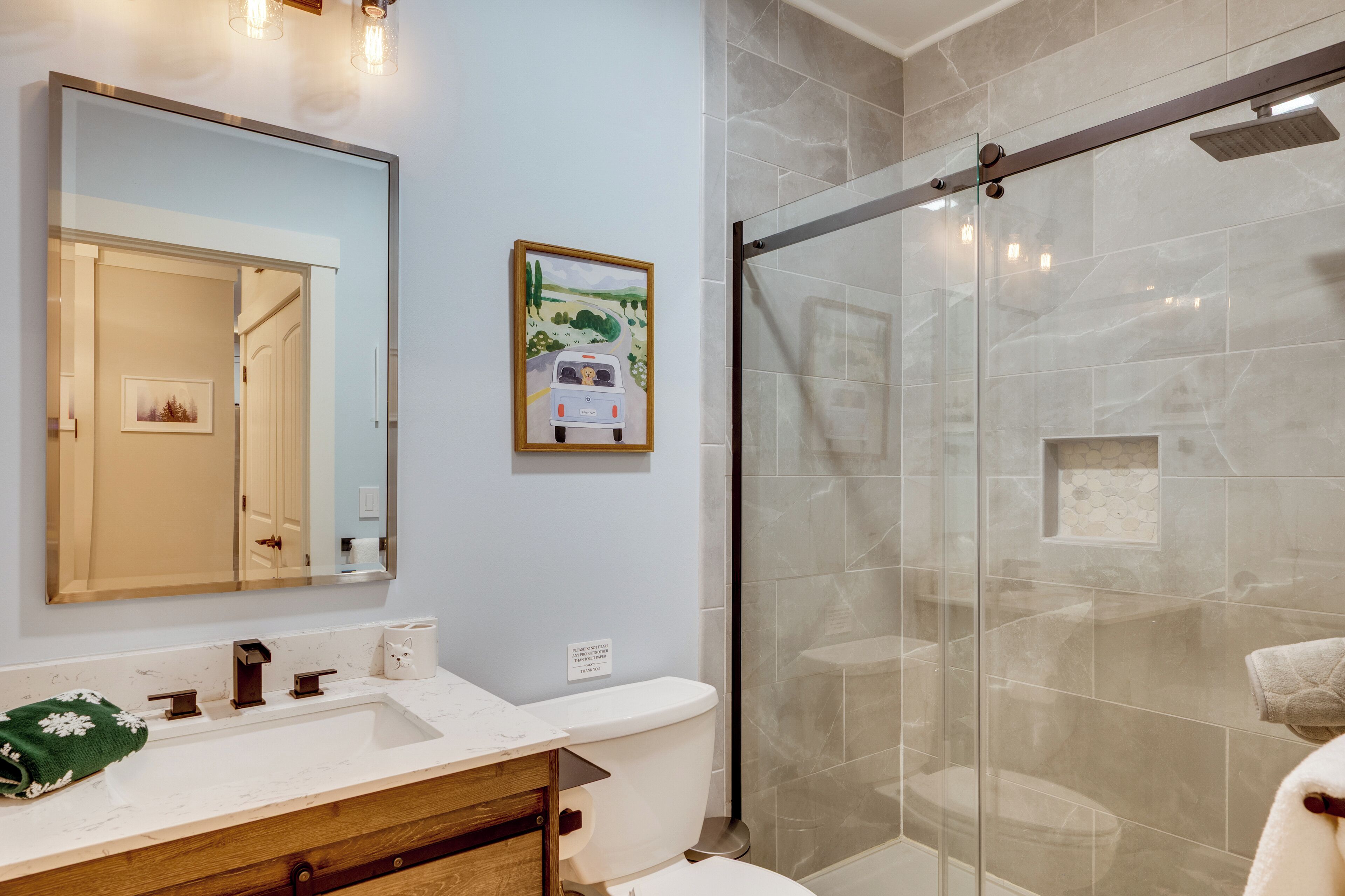 A bathroom with a large mirror, a sink, a toilet, and a glass shower enclosure.
