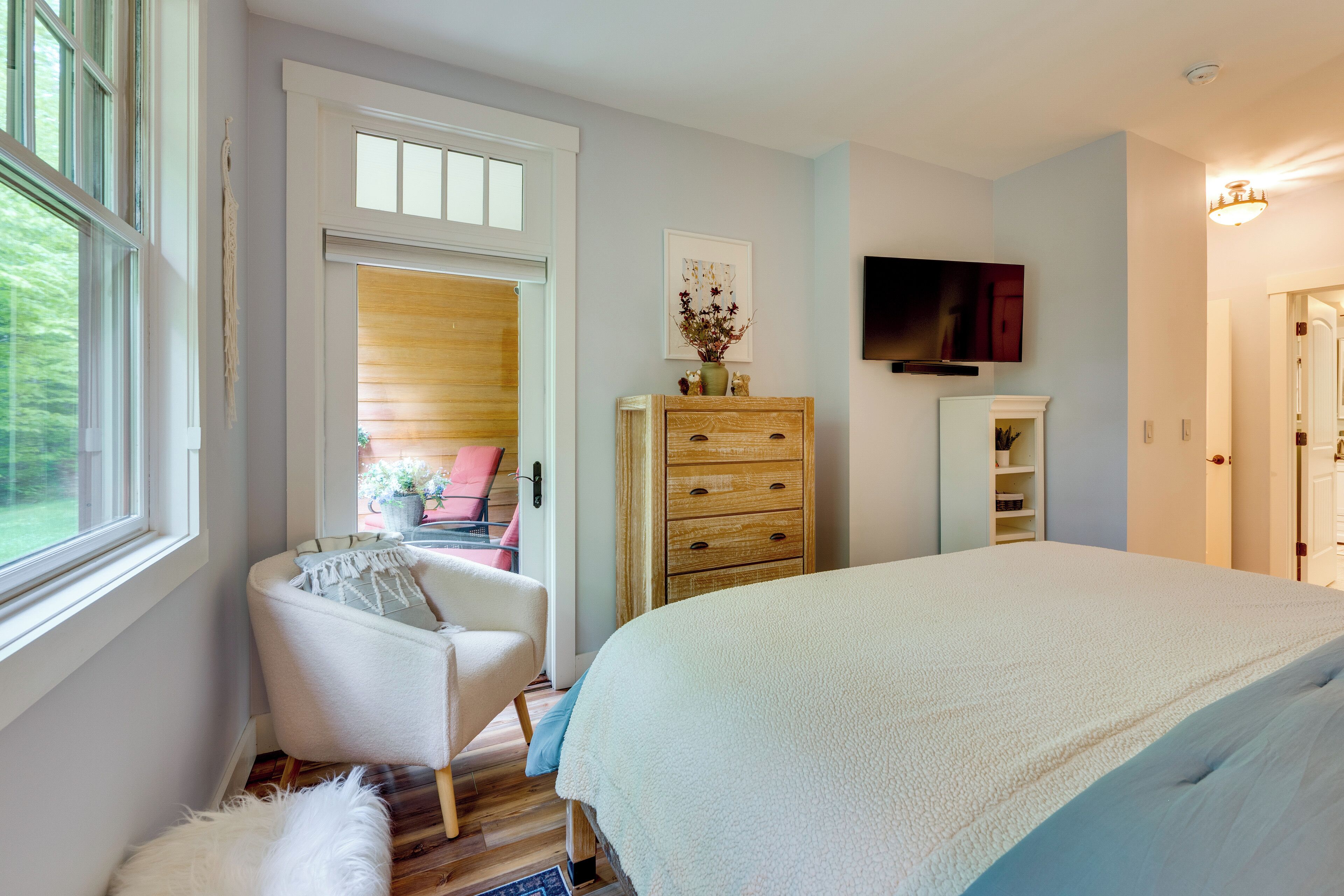 A bedroom with a large bed, a chair, a dresser, a television, and a door leading to another room.