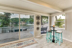 Ein Zimmer mit einer großen Schiebetür und Zugang zu einer Terrasse, einem kleinen Tisch mit Hockern sowie dekorativer Wandgestaltung.