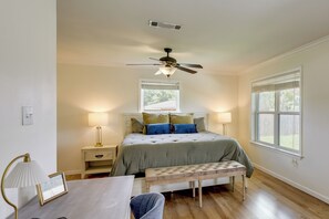 Une chambre à coucher comprenant un lit, des tables de chevet, un ventilateur de plafond, une fenêtre et un banc.