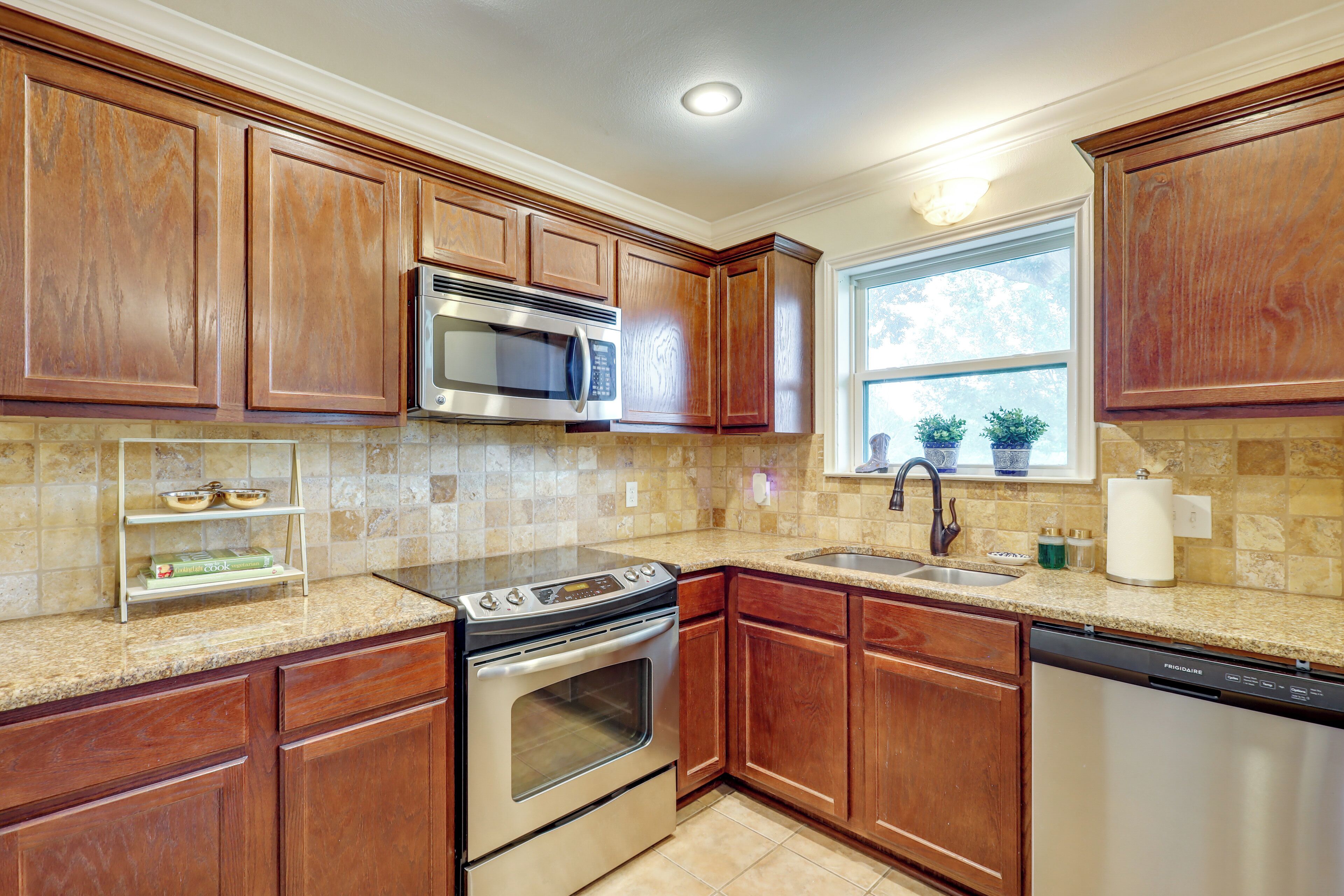 A kitchen with wooden cabinets, stainless steel appliances, a granite countertop, and a window with a view.
