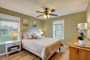 Une chambre à coucher avec un lit, des tables de chevet, un ventilateur de plafond et des fenêtres.