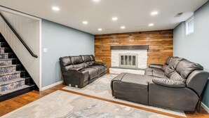 A living room with a fireplace, a sofa, a recliner, and a staircase. - Spacious Home: Private Deck 4 Mi to Dtwn Fargo (Moorhead)