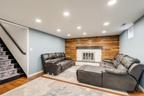 Un salon avec une cheminée, un canapé, un fauteuil inclinable et un escalier.