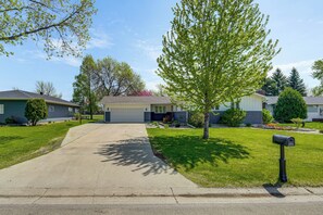 A residential driveway leading to a house with a garage, surrounded by well-maintained lawns and trees.