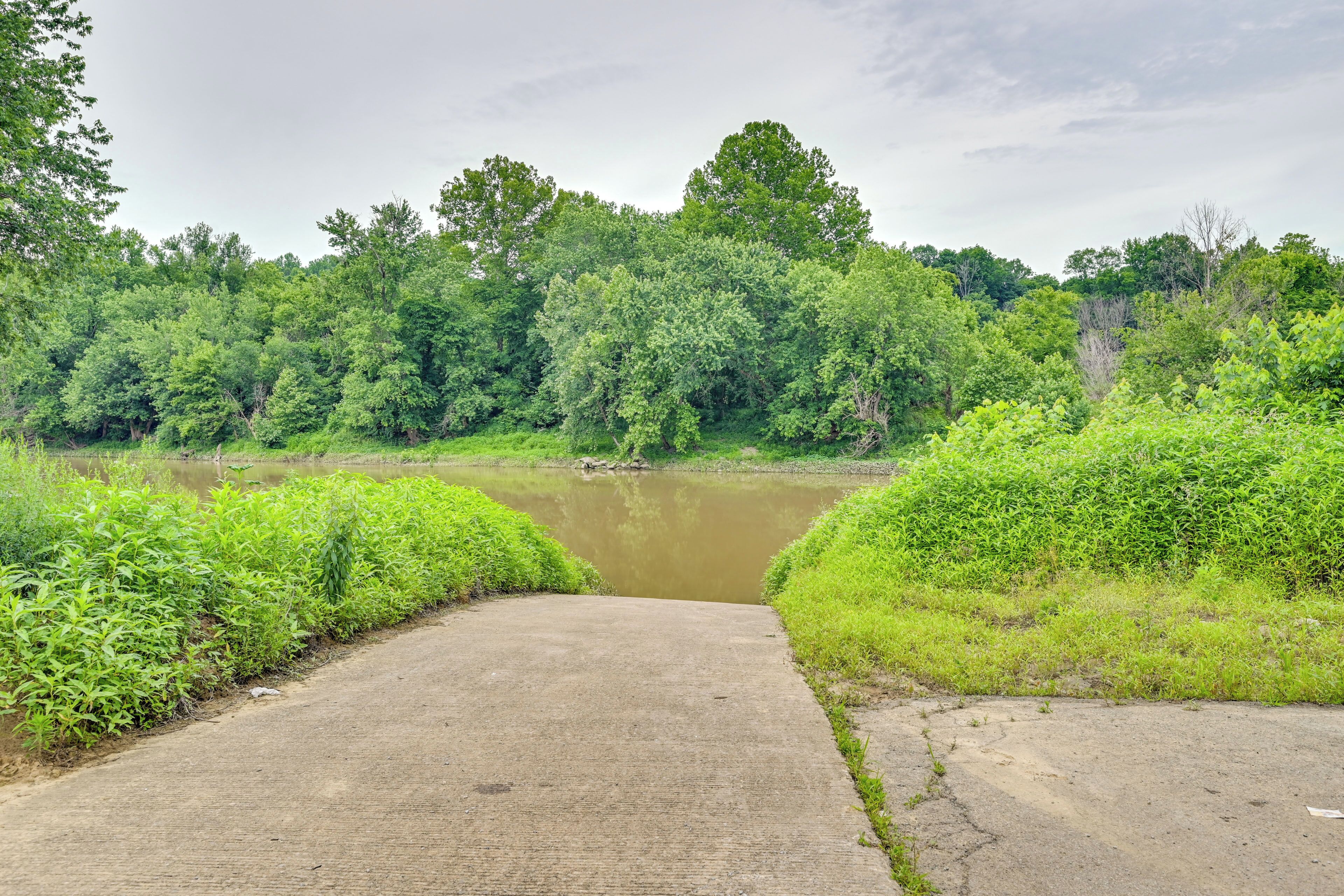 A concrete pathway leading to a body of water surrounded by dense greenery.