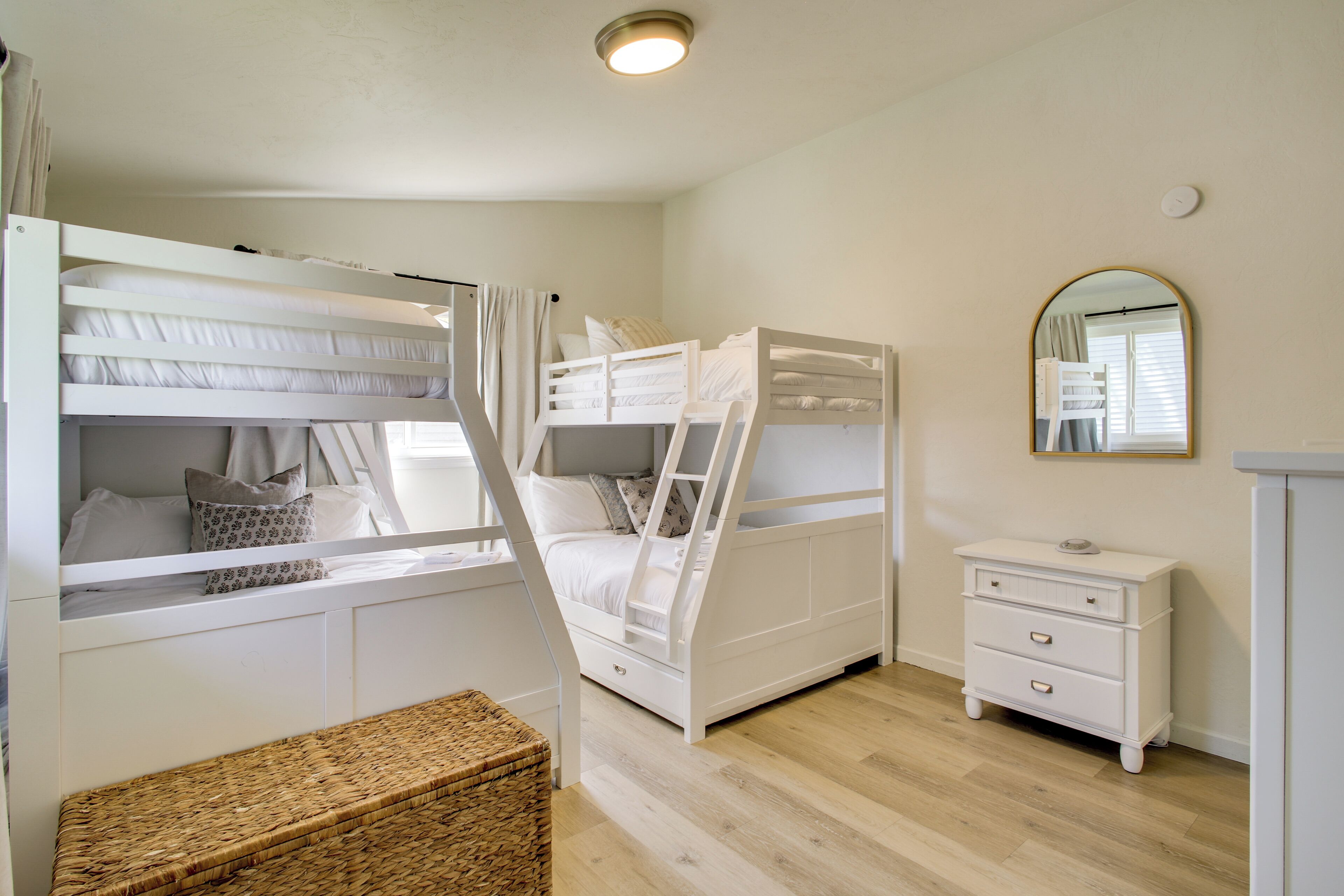 A bunk bed room with a mirror, a dresser, and a wicker basket.