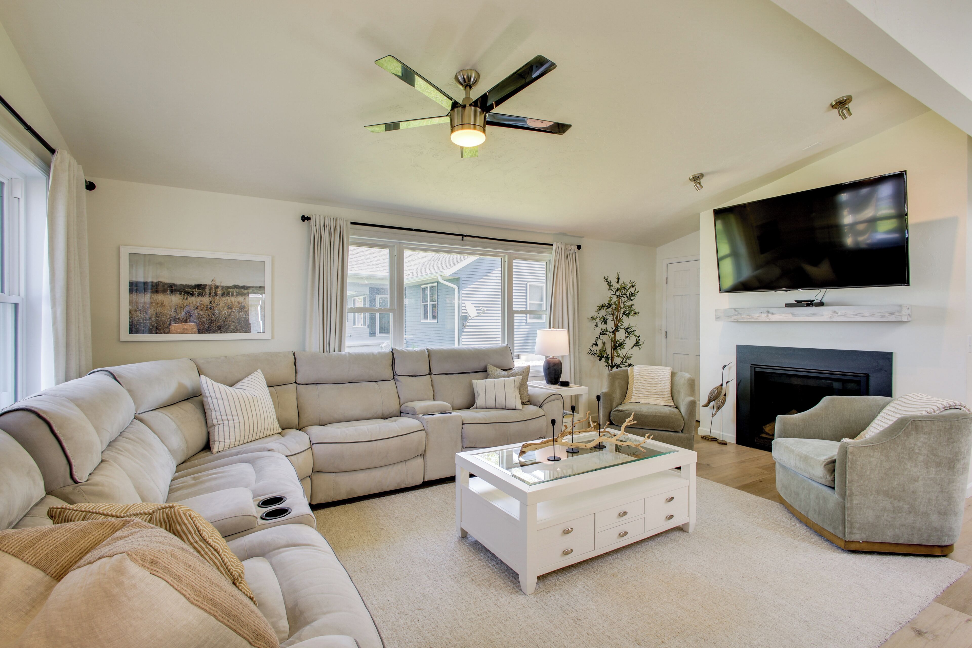 Ein Wohnzimmer mit Ecksofa, Glastisch, Kamin und Wand-Fernseher.