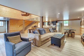 A spacious living area with a sofa, armchair, ottoman, and a dining table with chairs. A staircase is visible in the background leading to an upper level. - Jurassic Retreat: Hot Tub & Life-size Dinosaurs! (Washougal)