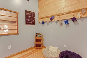 A room with a wooden floor, a bed, a shelf with toys, a wall-mounted picture, and a window with blinds. - Jurassic Retreat: Hot Tub & Life-size Dinosaurs! (Washougal)