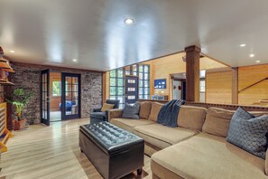 A modern living room with a sectional sofa, a leather ottoman, and a stone wall. - Jurassic Retreat: Hot Tub & Life-size Dinosaurs! (Washougal)