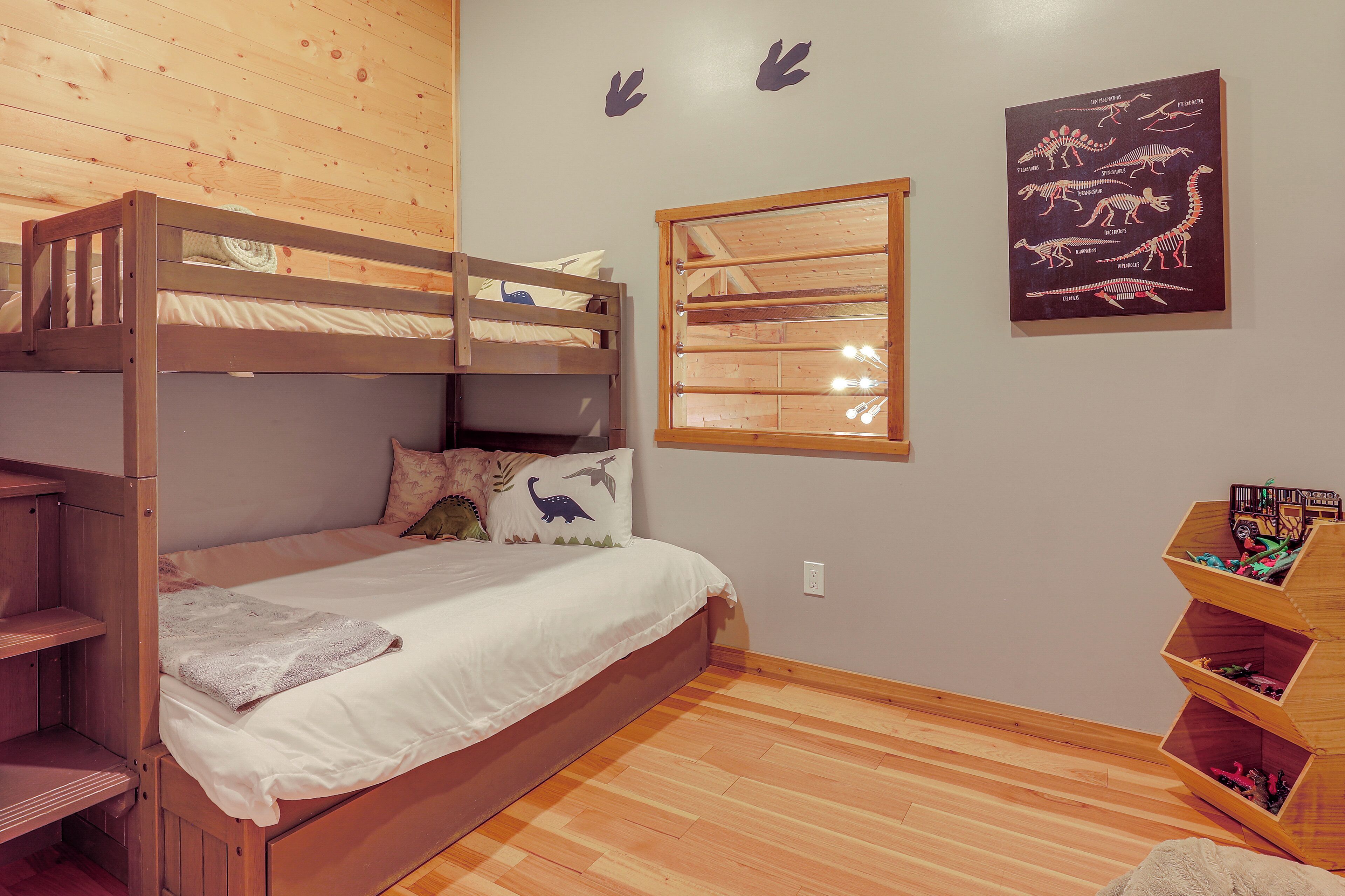 Habitación con literas, una ventana, estantes de madera y decoración de pared con temática de dinosaurios.