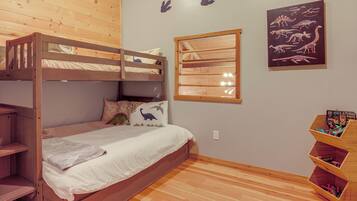 Habitación con literas, una ventana, estantes de madera y decoración de pared con temática de dinosaurios.