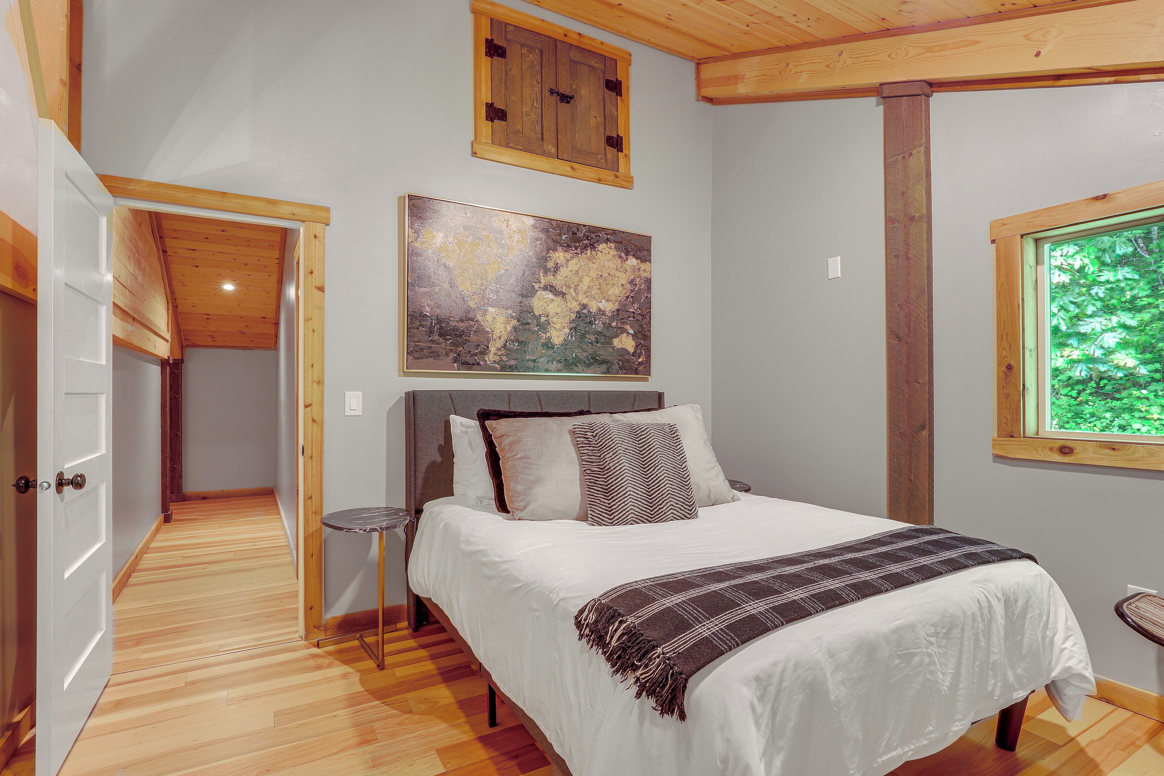 A bedroom with a bed, a painting, a window, and a door.