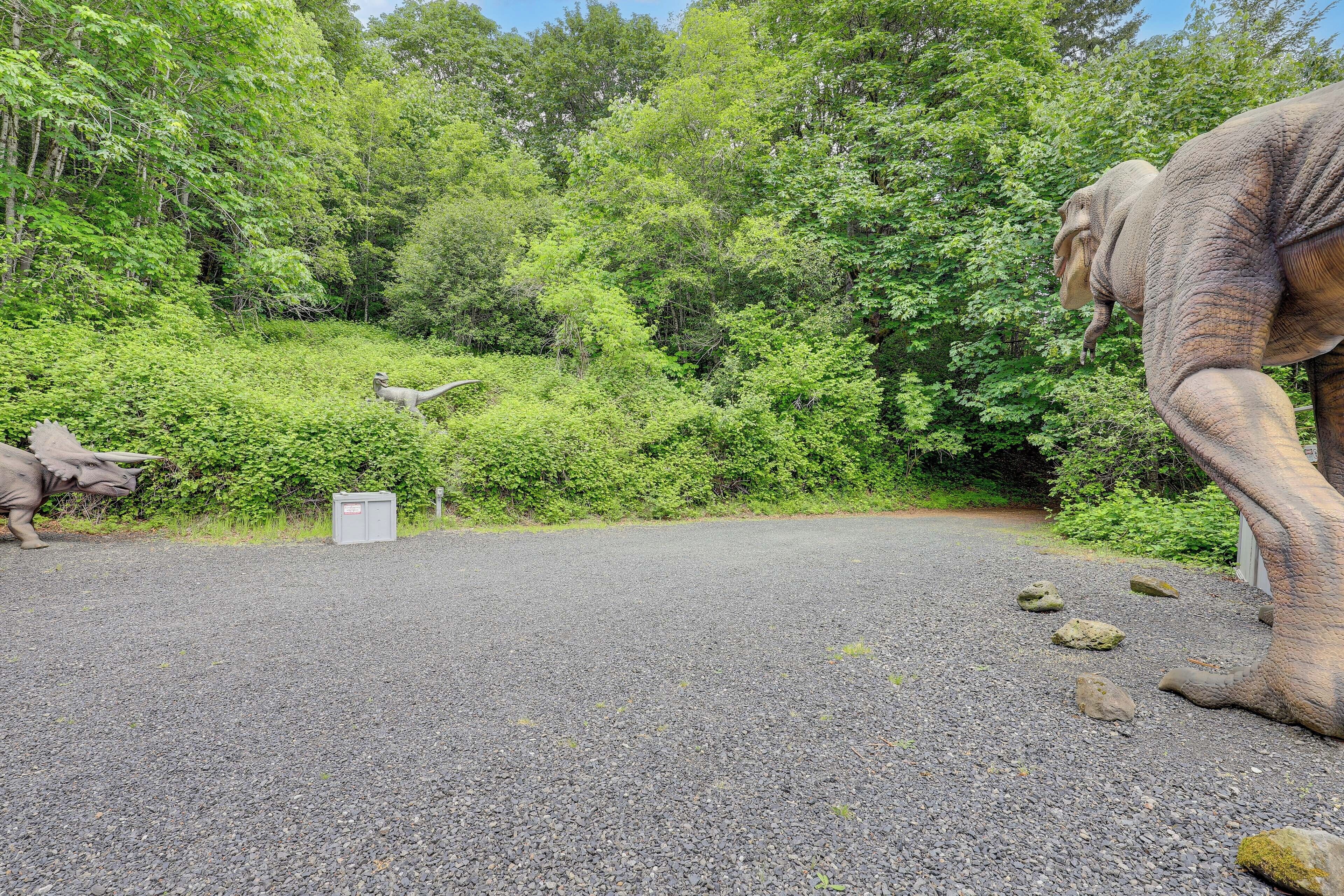 A paved area with a large elephant statue, a dinosaur statue, and dense green foliage in the background.