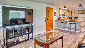 A modern kitchen with bar stools, a dining table, and a TV in the living area. - Stunning View! Peaceful Family Home w/ Yard in Roy (Roy)
