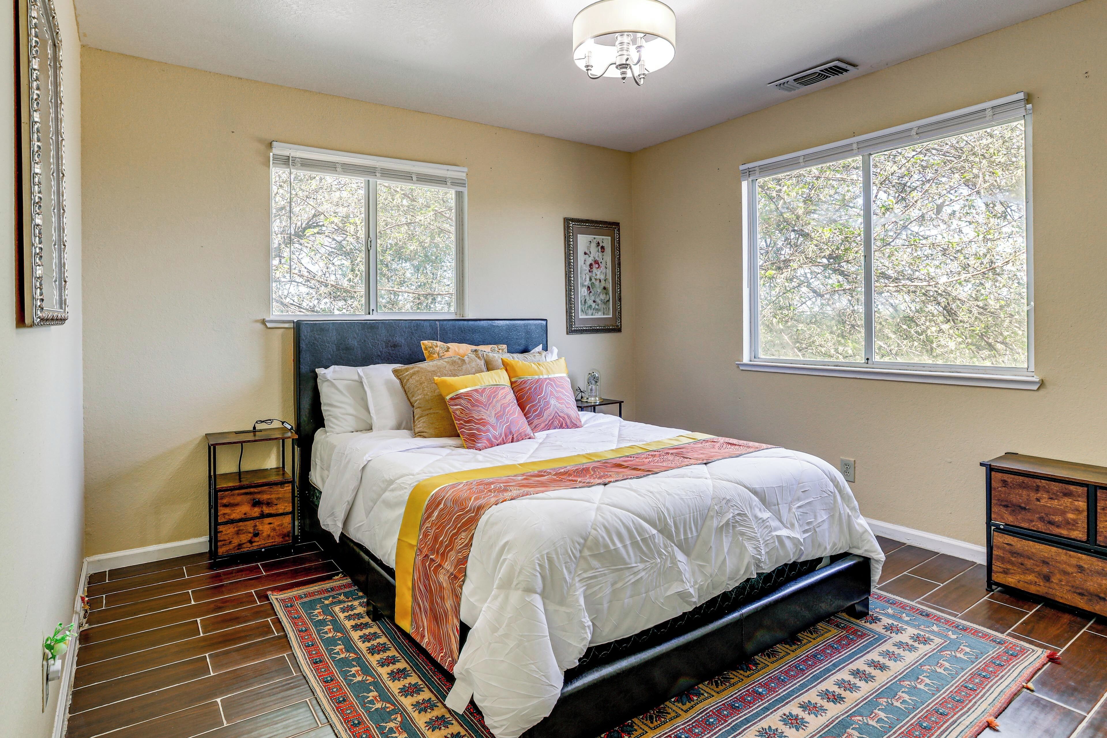 A bedroom with a bed, two windows, a nightstand, a dresser, and a patterned rug.