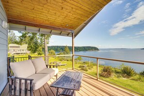 Una terraza techada con sofá y mesa, con vista a un lago y un bosque.