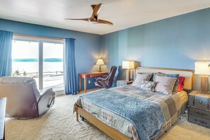 Un dormitorio con cama, escritorio, silla, maleta y vistas al exterior.