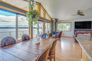 A spacious dining area with a large table, chairs, and a hanging plant. - South-facing Herron Island Retreat w/ Sound Views! (Lakebay)