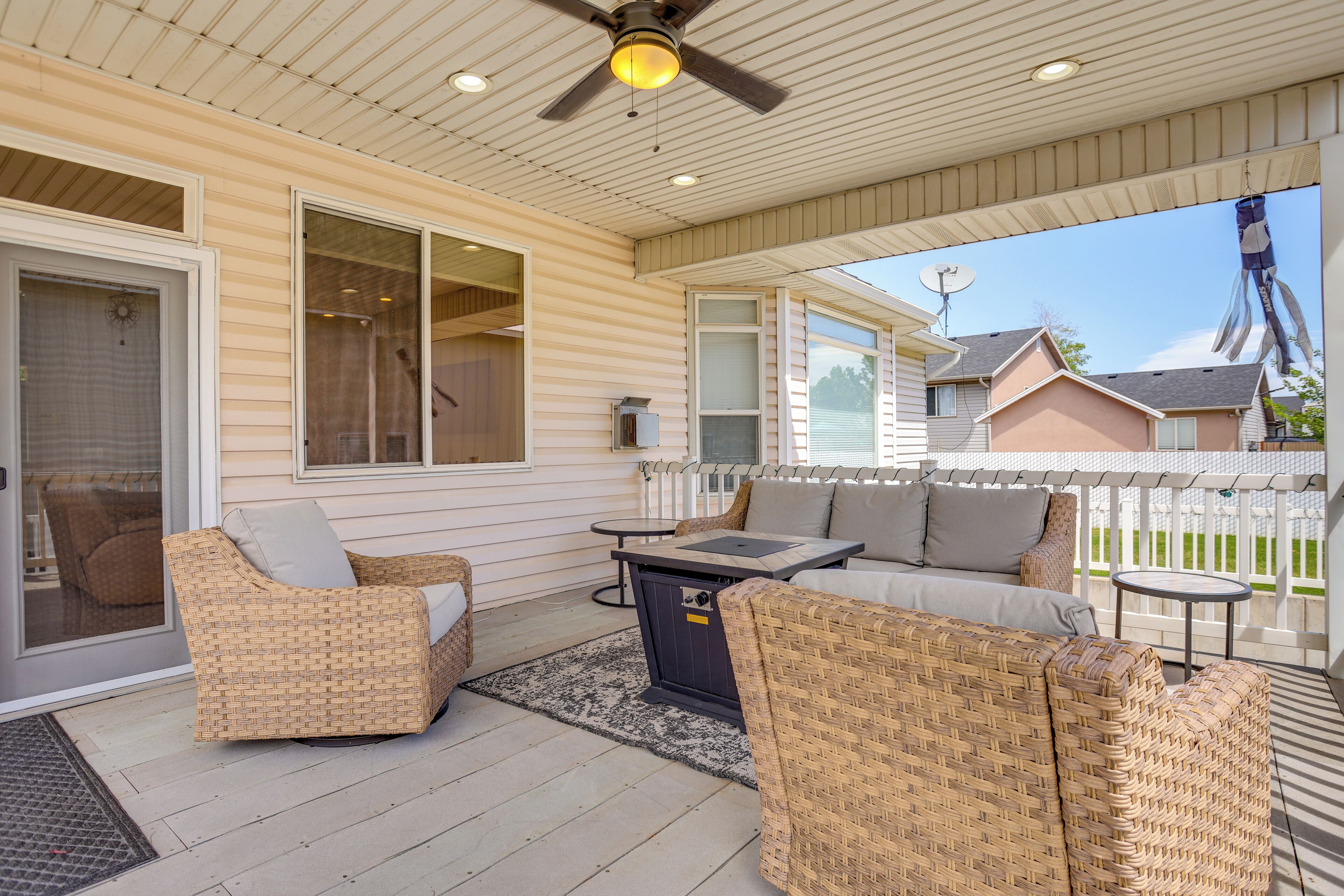 A covered patio with wicker furniture, a ceiling fan, and a view of neighboring houses.