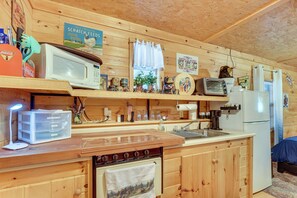 Puinen mökki, jonka keittiössä on liesi, mikroaaltouuni, jääkaappi ja erilaisia keittiötarvikkeita.