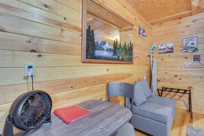 A wooden cabin interior with a table, a fan, a chair, and a painting of a mountain landscape. - Smoky Mtn Tiny Cabin Hideaway: Hot Tub, Patio (Englewood)
