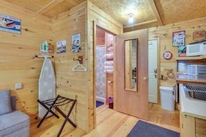 A wooden cabin interior with a kitchenette, a drying rack, a mirror, and a door leading to a bathroom. - Smoky Mtn Tiny Cabin Hideaway: Hot Tub, Patio (Englewood)