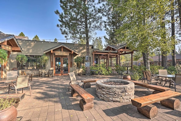 An outdoor patio area with wooden benches, a stone fire pit, and a covered seating area. - Resort Pool & Trails! Cozy Seventh Mountain Condo (Bend)