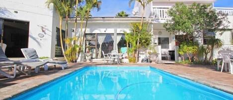 A swimming pool with lounge chairs, palm trees, and a white building with multiple windows and balconies.