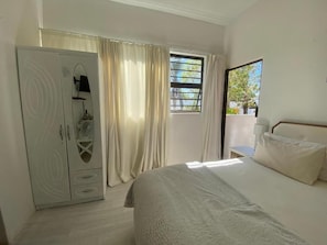 A hotel room with a bed, a wardrobe, a window with curtains, and a view of greenery outside.